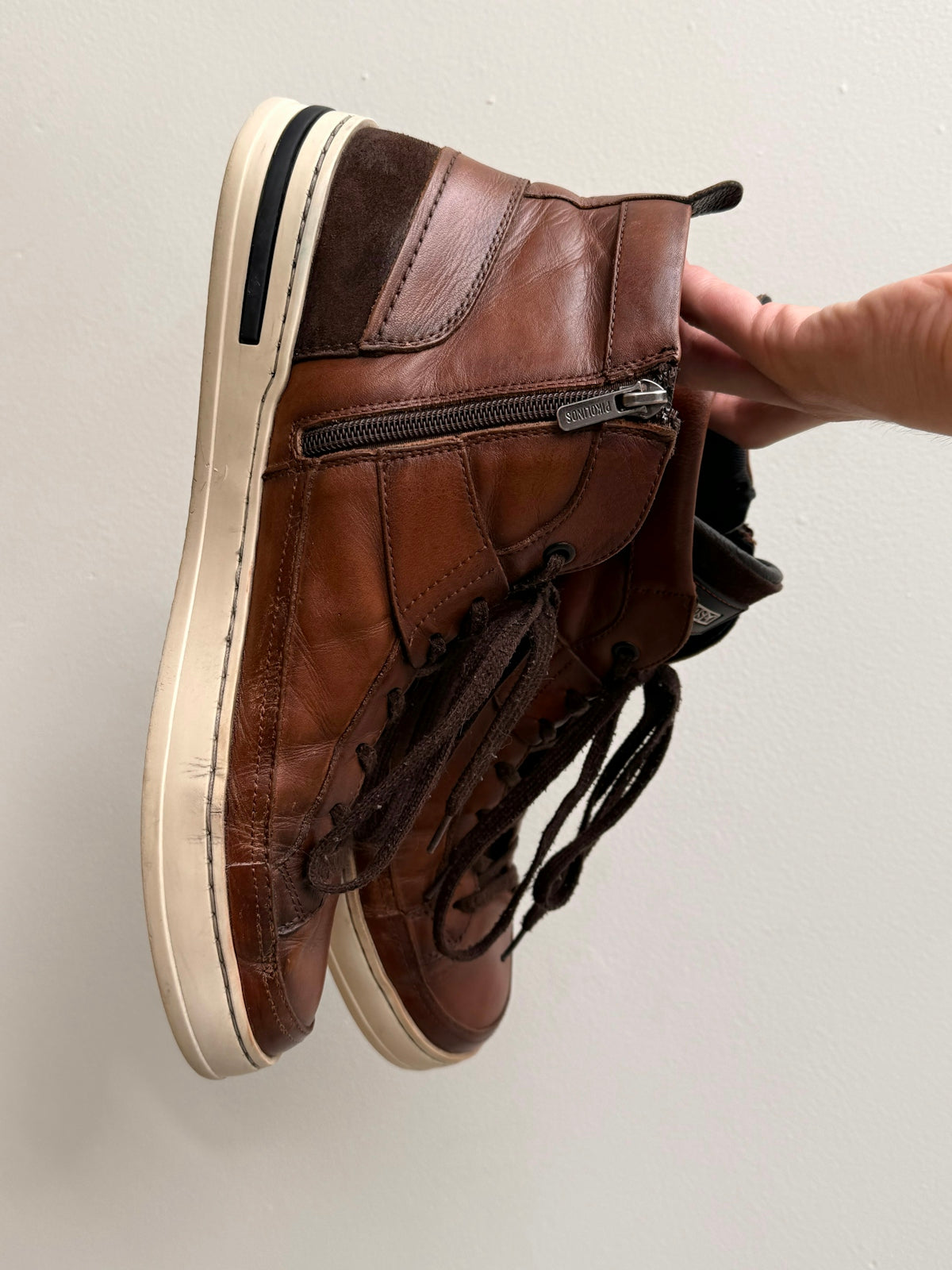 A person holds a pair of brown leather high-top sneakers