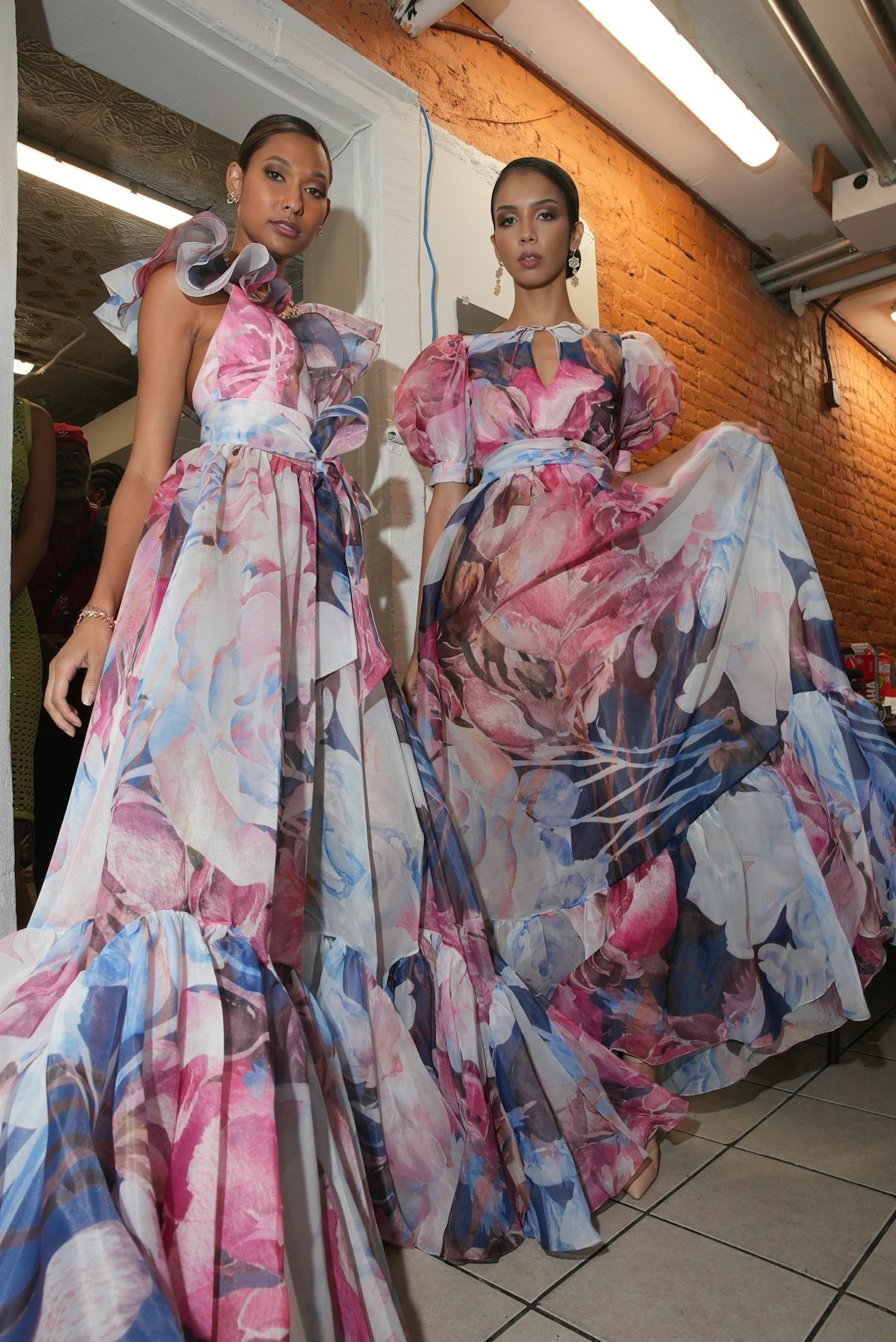 Two women wearing elegant floral print gowns.